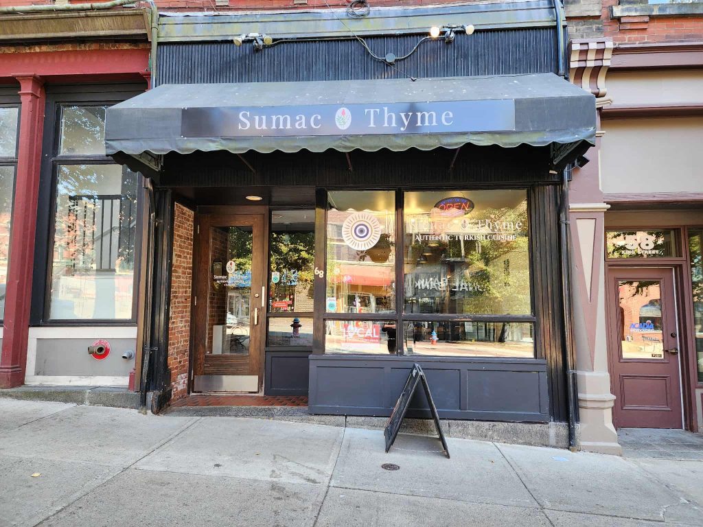 The exterior of Sumac & Thyme on King Street in Uptown Saint John, with a black awning, brick details, and large front windows.