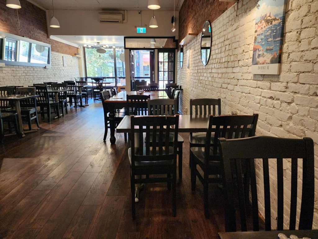 Inside Sumac & Thyme restaurant showing wooden floors, whitewashed brick walls, black chairs, and natural light streaming in from the front windows.