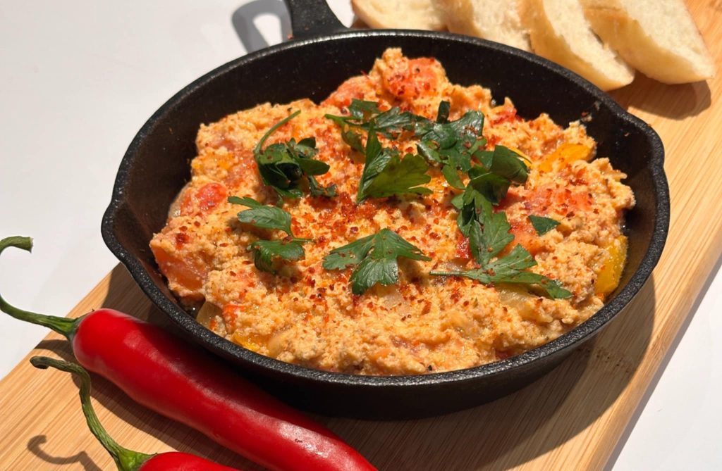 A black cast iron skillet filled with a delicious Turkish dish, garnished with parsley and chili flakes, served with fresh bread and red chili peppers on the side.