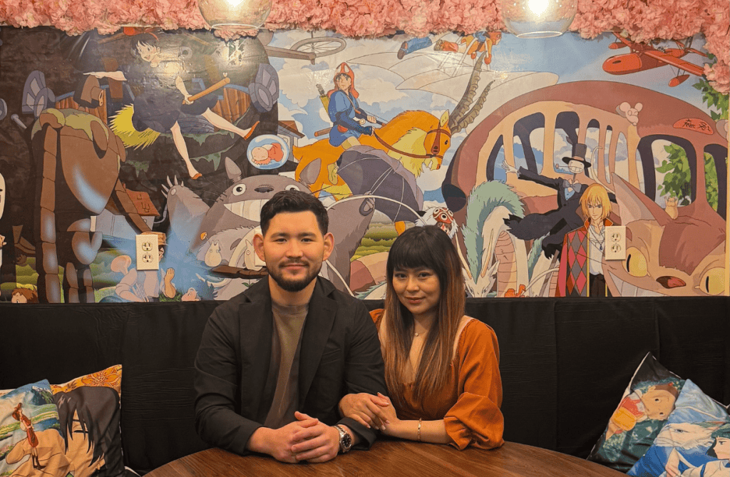 Owners Eunice Gale and Sanat Gabdyssamet sitting inside Umami Kid in Uptown Saint John, surrounded by anime-inspired wall art and cherry-blossom décor.