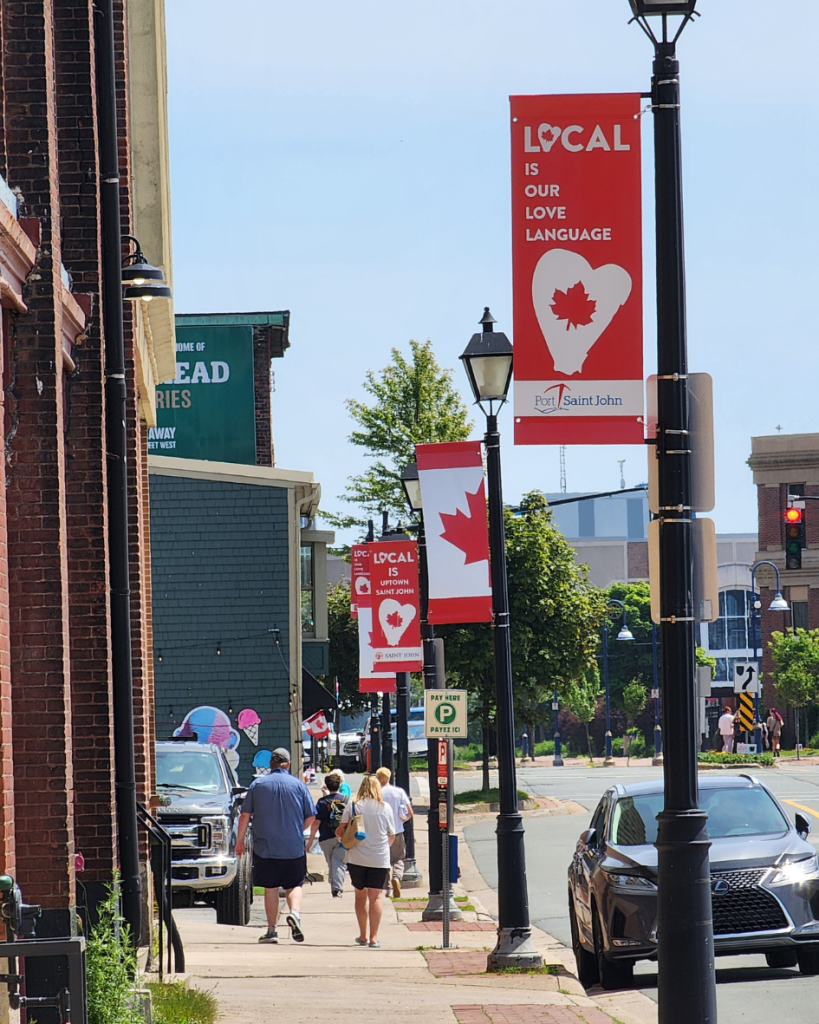 Local Love street banners displayed along an Uptown Saint John sidewalk during summer, celebrating local pride and placemaking.