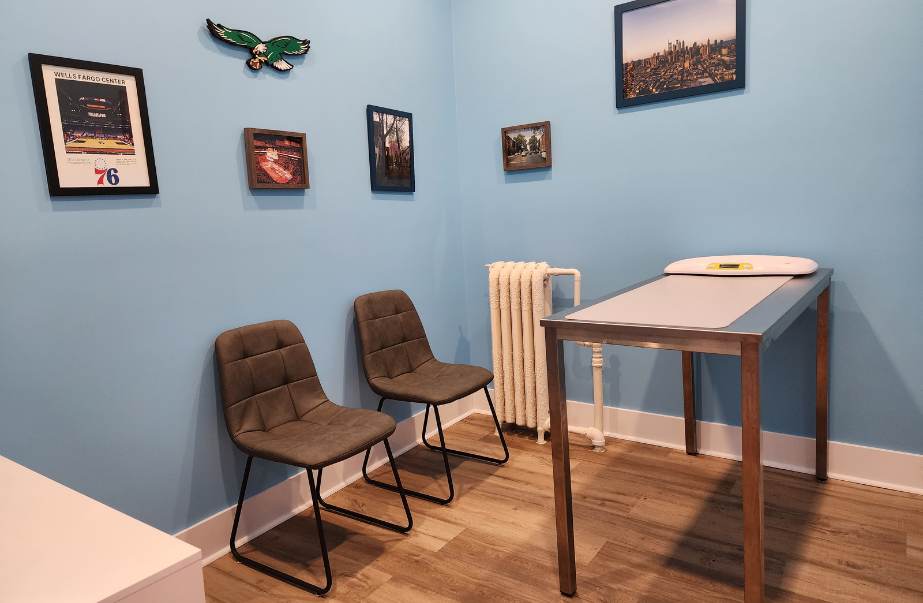 Blue exam room inside Uptown Animal Clinic with chairs, exam table, and framed wall art.